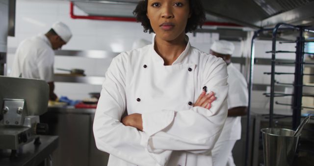 An experienced head chef standing confidently in a vibrant professional kitchen wearing a white uniform. Other kitchen staff is busy working in the background. Ideal for use in articles, blogs, or advertisements focused on culinary arts, restaurant management, teamwork, leadership, or professional kitchens.