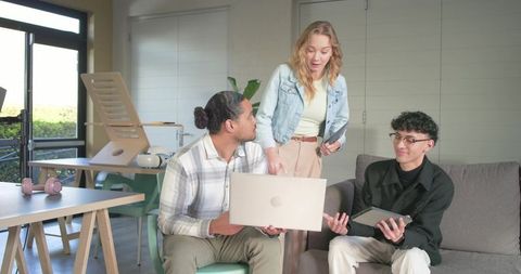 Diverse young professionals collaborating around laptop and tablet in modern workspace