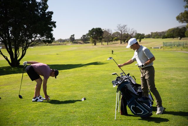 Two Caucasian male golfers practicing on a golf course on a sunny day wearing caps and golf clothes, preparing for game taking clubs out of a golf bag. Hobby healthy lifestyle leisure.