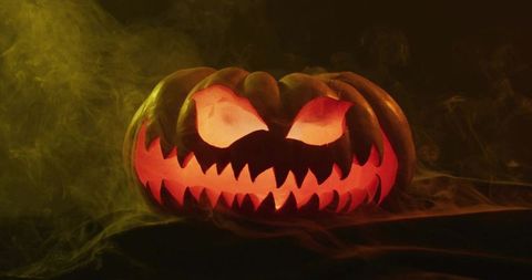 Glowing jack-o'-lantern casting eerie orange light through jagged mouth and arched eyes