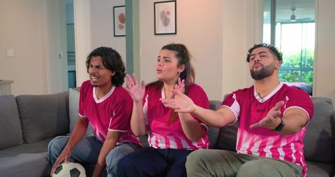 Friends reacting to tense soccer match on couch wearing red and white jerseys