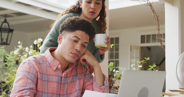 Image of biracial couple using laptop in the garden. Domestic lifestyle and leisure time at home.