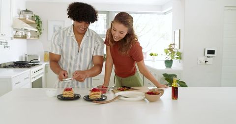 Happy Couple Preparing Pancakes with Strawberries in Modern Kitchen