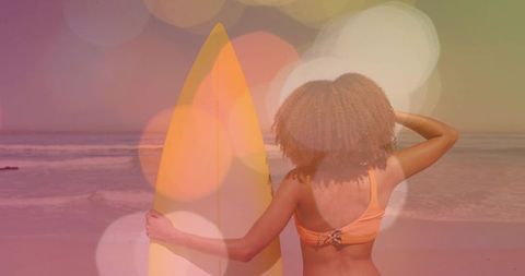 Sunset surf pose with yellow board and curly-haired woman in peach bikini