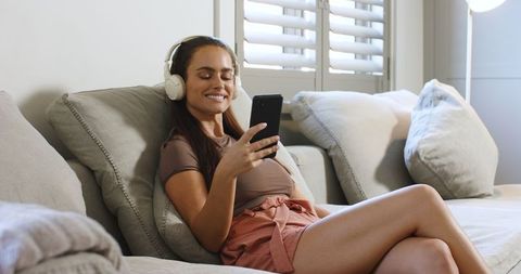 Woman Relaxing on Sofa with Wireless Headphones and Smartphone at Home