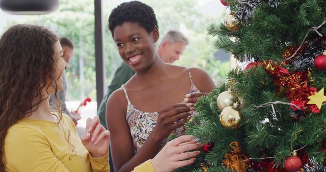 Diverse friends decorating Christmas tree, sharing joyful moment. Great for holiday-themed marketing, festive season promotions, family and friends gatherings, and emphasizing diversity and joy during holidays.