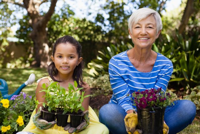 Grandmother and granddaughter sitting together in backyard, smiling while holding potted plants. Scene depicts bonding moment, family activity, and love for gardening. Perfect for illustrating family relationships, gardening hobbies, and outdoor activities.