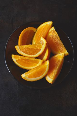 Fresh orange wedges showcasing vibrant citrus color on black plate with dark backdrop