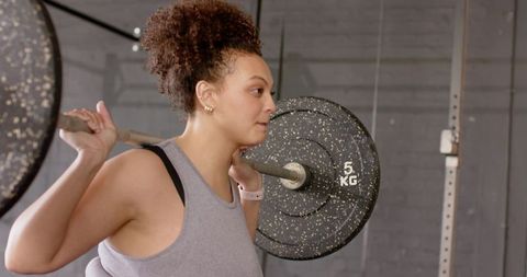 Female athlete lifting barbell across shoulders at gym, focused strength training workout