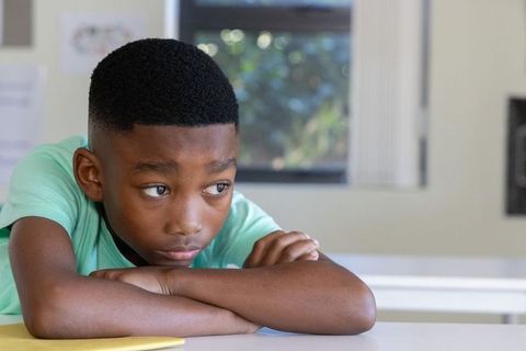 Contemplative african american boy resting on arms looking out window in classroom light