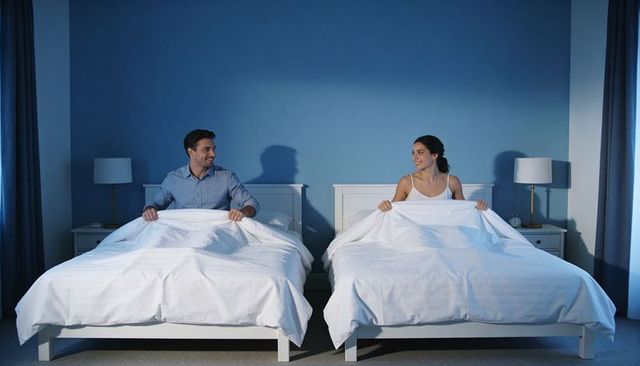 Couple in separate twin beds sharing warmth and smiles in cozy blue bedroom at night