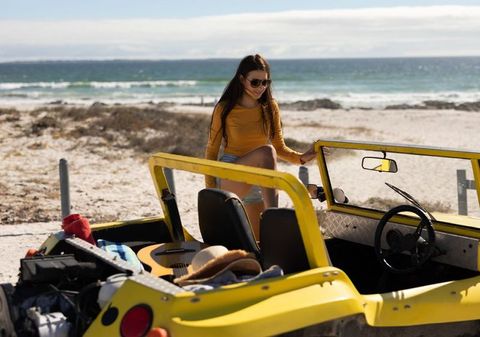 Woman enjoying beach day with yellow dune buggy by ocean