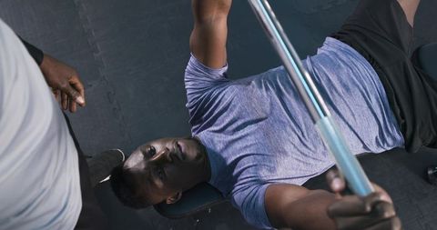 Two men engaged in barbell bench press workout at gym