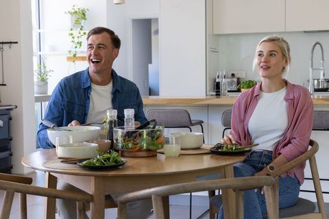 Couple laughing and sharing healthy salad at bright modern kitchen table