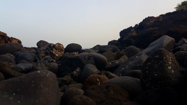 Close-up shot of a rocky shoreline showing various sizes of stones under a dusky sky. Suitable for themes related to nature, tranquility, self-reflection, and natural landscapes. Ideal for use in travel brochures, environmental campaigns, meditation guides, and background images in presentations.
