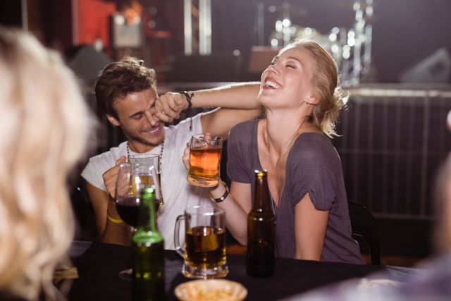 Cheerful friends holding beer mugs while sitting at nightclub