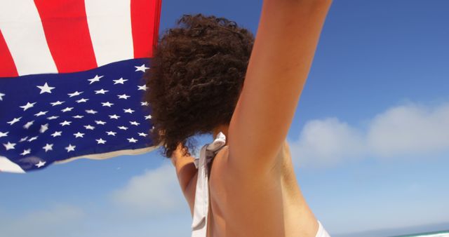 Excited girl celebrating Independence Day by holding the American flag on a beach. Perfect to use in any materials related to patriotism, summer holidays, Fourth of July promotions, and outdoor beach activities.