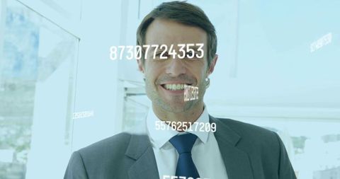 Smiling businessman presenting numeric overlays on glass windows in modern office environment