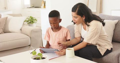 Caregiver guiding child using tablet for learning in sunlit living room