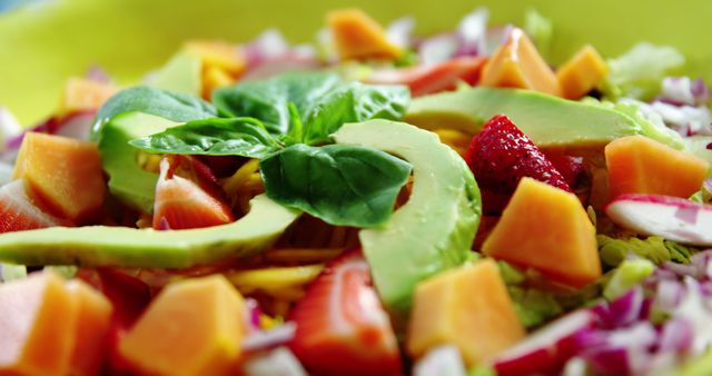 This vibrant, close-up image of a healthy salad featuring avocado slices, papaya cubes, strawberries, and fresh basil on a bed of greens is perfect for promoting nutritious and delicious meal ideas. Ideal for use in health and wellness blogs, vegan recipes, menu designs, cooking websites, and diet-centric promotions.