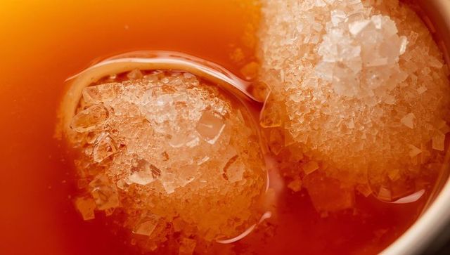Crushed ice spheres melting in amber cocktail close-up, frosted crystal beads on cup rim
