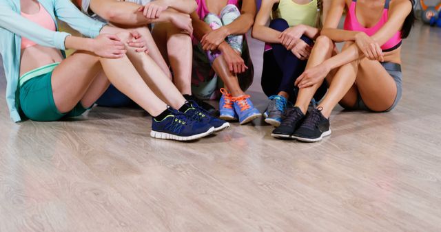 A group of fit individuals are sitting together on the gym floor, resting after a strenuous workout. They are wearing colorful sportswear and sneakers, creating a vibrant scene of camaraderie and team spirit. This image is ideal for fitness blogs, gym promotions, and wellness social media campaigns.
