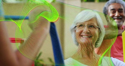 Smiling senior woman exercising with resistance band on outdoor patio group fitness