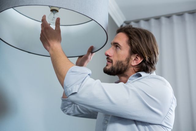 Man installing a light bulb in a modern living room. Ideal for use in articles or advertisements related to home improvement, DIY projects, interior design, and household maintenance.