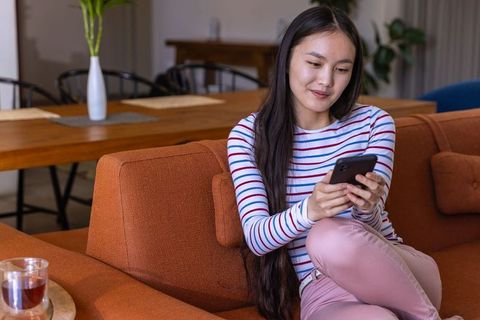 Woman relaxing on sofa at home with smartphone