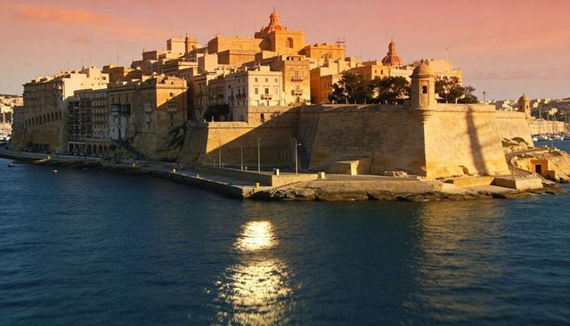 Valletta limestone bastions bathing in golden sunset, harbor waters reflecting warm light