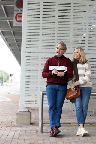 Senior couple standing at covered bus stop waiting with notebook and leather bag