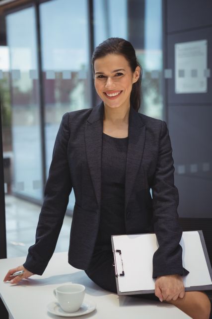 Portrait of businesswoman with clipboard sitting on the desk at office