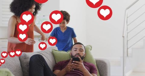 Man Relaxing on Sofa Engaged with Social Media While Heart Icons Surround