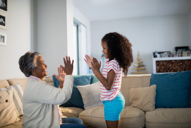 Grandmother and granddaughter enjoying a playful clapping game in a cozy living room. Perfect for illustrating family bonding, intergenerational relationships, and joyful moments at home. Ideal for use in family-oriented advertisements, parenting blogs, and lifestyle articles.