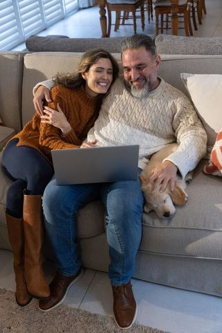 Couple cuddling on sofa using laptop with sleeping puppy on lap cozy home moment
