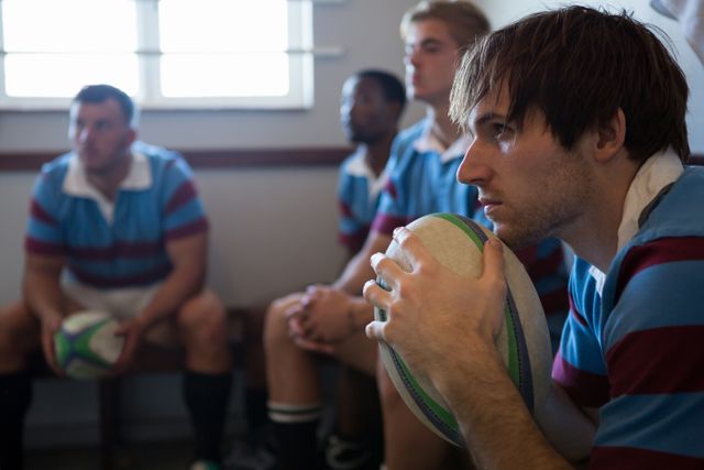 Close up of thoughtful rugby team looking away while sitting in locker room