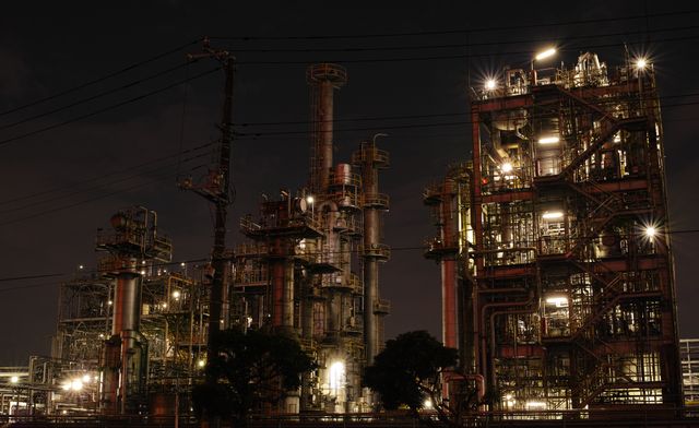 This depicts a large industrial refinery plant at night with illuminated infrastructure and machinery. It shows a complex network of pipes, towers, and various industrial equipment, highlighting the scale of energy production and manufacturing. Suitable for use in topics related to industry, engineering, manufacturing, and energy production. It can be used in articles, reports, educational materials, promotional content, and informatics related to industrial processes, energy facilities, and technological advancements in the industrial sector.