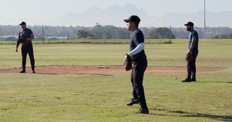 Three baseball teammates standing on sunlit field preparing for play and training drills