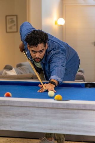 Curly-haired man leaning over pool table aiming precise shot wearing jacket smartwatch