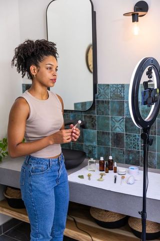 African american creator filming skincare routine with ring light in bathroom vanity