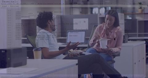 Coworkers talking and eating takeout while reviewing code on laptops in modern open office