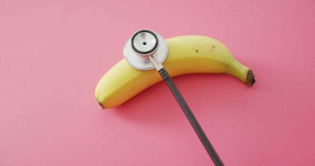 Image of fresh banana with stethoscope with copy space on pink background. fusion food, fresh fruit and healthy eating concept.