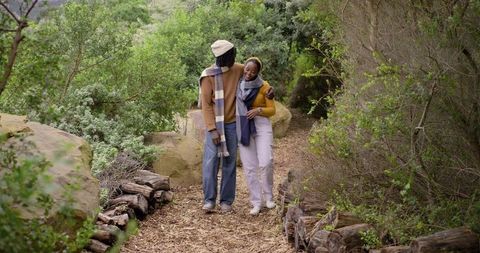 African american couple walking arm-in-arm on nature trail wearing scarves and beanie