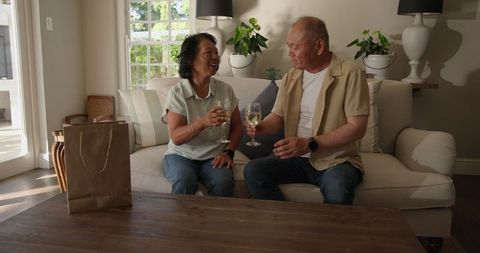 Senior asian couple enjoying wine and laughter in living room