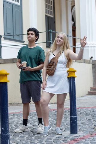Diverse young friends standing on cobblestone street waving and checking phone