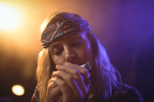 Female musician passionately playing harmonica in a nightclub with colorful lighting. Ideal for use in articles, blogs, and advertisements related to live music, nightlife, entertainment, and artistic performances.