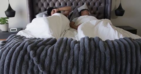 Two men lying together in modern bedroom sharing white duvet and chunky gray knit blanket
