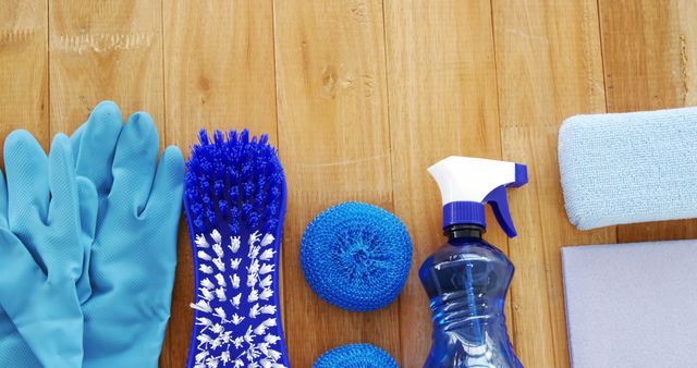 Cleaning supplies including blue rubber gloves, a variety of scrub brushes, and a spray bottle are neatly arranged on a wooden surface, with copy space. These items are essential for maintaining cleanliness and hygiene in domestic or professional settings.