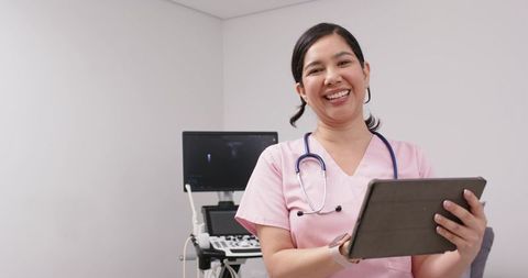Smiling nurse holding tablet next to ultrasound machine in bright clinic exam room