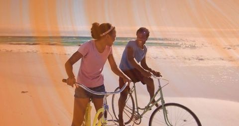 Couple cycling on beach at sunset with lens flare